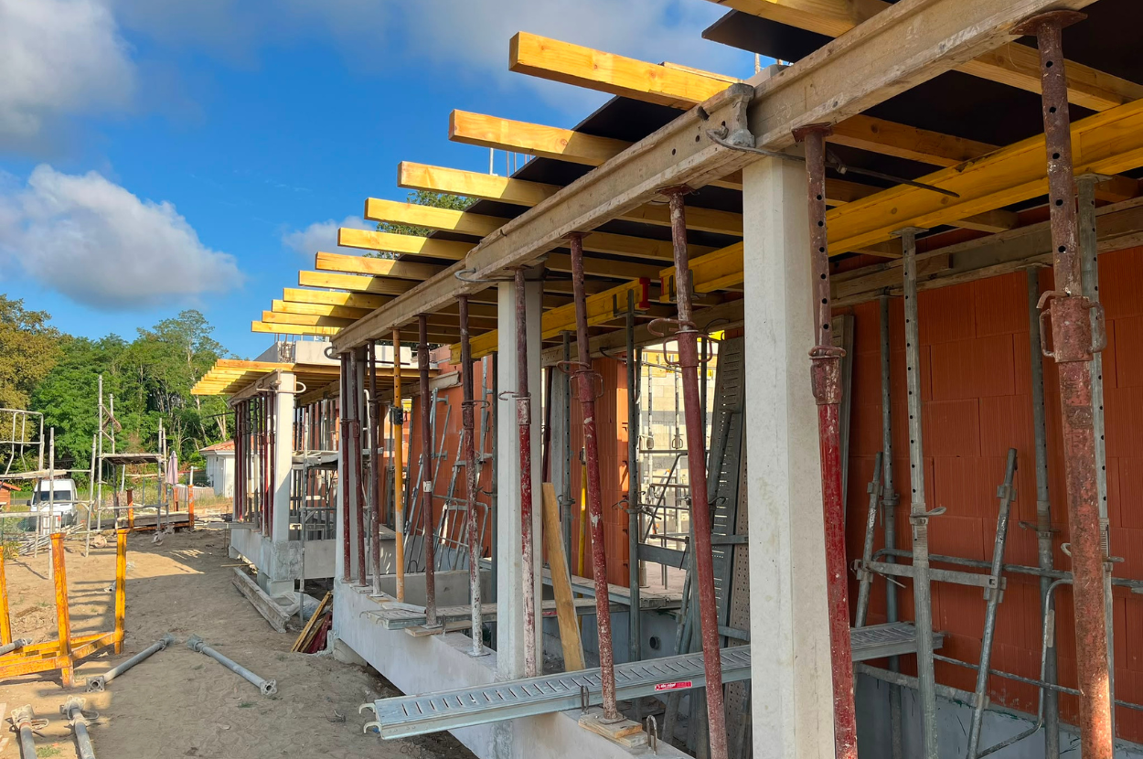 Structure de maison en construction avec ossature en bois, poutres jaunes et murs en béton non finis